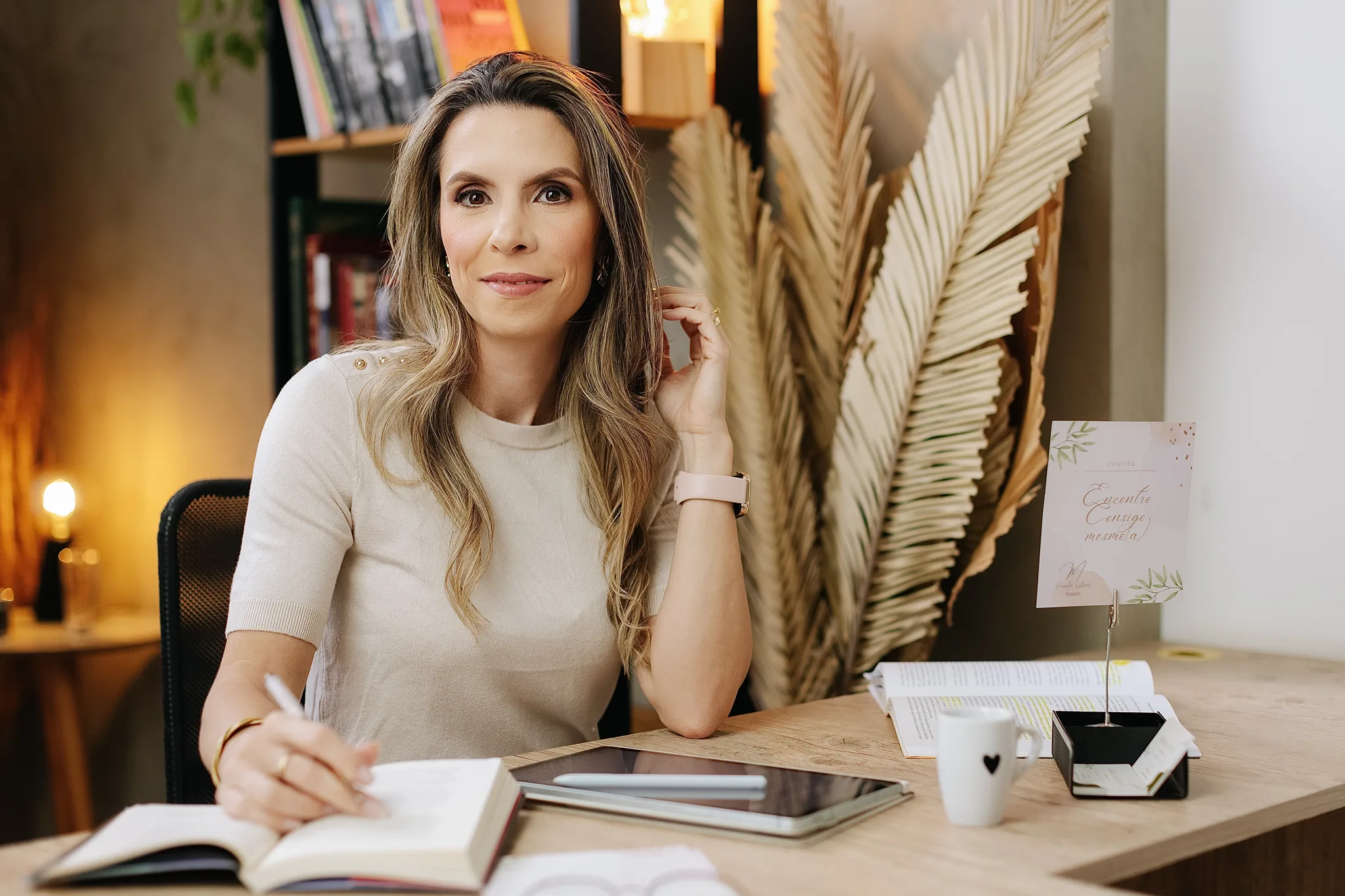 Mirela Esteves sentada à mesa do consultório, com um livro aberto
